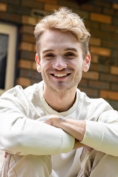 Portrait of happy 22 years old young man sitting front of the house, background with copy space, full frame horizontal composition